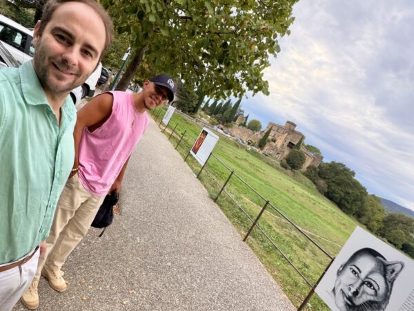 Deux personnes devant les panneaux de l’exposition de Rocally, avec le pré de la Plantade et le château de Lourmarin en arrière-plan.